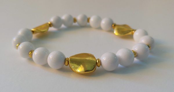 Elastiskt armband med vit jade, guldfärgade asymmetriska mellandelar och guldfärgade minirondeller. 